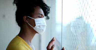 Pencere kenarında duran Afrikalı kadın virüse karşı salgın maskesi takıyor.