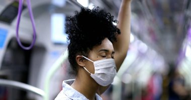 Metroda giderken elinde tırabzan, yüzünde maske olan genç siyahi bir kadın.