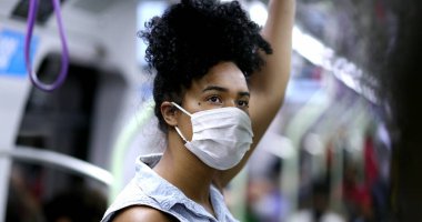 Metroda giderken elinde tırabzan, yüzünde maske olan genç siyahi bir kadın.