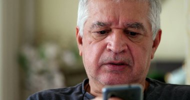 Evde cep telefonu kullanırken hayal kırıklığına uğramış bir ihtiyar. Akıllı telefona bakan yaşlı kişi üzgün.