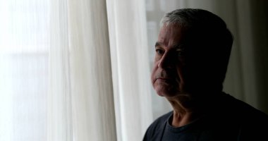 Depresyonda olan yaşlı adam, pencerenin kenarında gölgede duruyor.