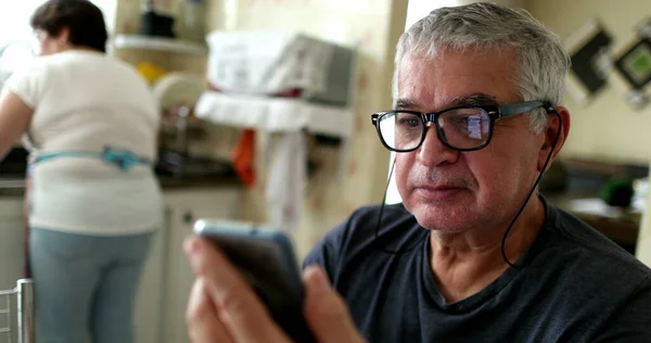 Casual older man reading content on smartphone device at home