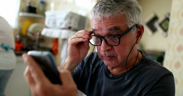 Senior man using smartphone putting reading glasses