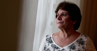 Evde pencerenin önünde duran üzgün yaşlı kadın. Depresyondaki endişeli 60 yaşındaki bayan