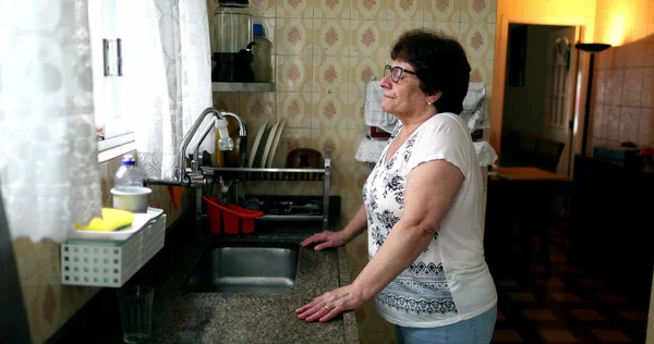 Pensive Older Woman Standing Kitchen Sink Home Thoughtful Lady 60S — стоковое фото
