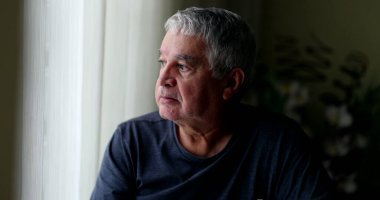 Bunalımda olan orta yaşlı bir adam evde oturup pencereden bakıyor.