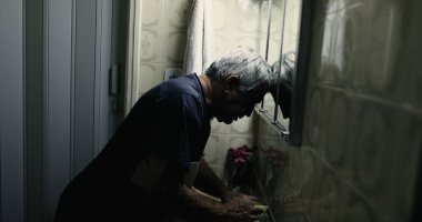 Çaresiz 60 yaşındaki adam, banyo aynasına yaslanmış keder ve umutsuzluk içinde.