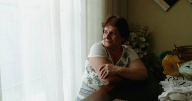 Evde pencereden bakan yaşlı bir kadın.