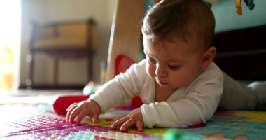 Bebek yerde uzanmış oyun hasırına dokunuyor, bebek dünyayı keşfediyor.