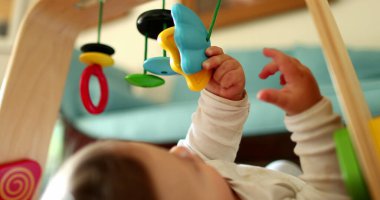 Bebek elleri oyuncak tutuyor, yakın plan bebek oyunları oynuyor ve yerde çocuk gelişimi var.