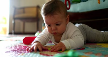 Bebek yerde uzanmış oyun hasırına dokunuyor, bebek dünyayı keşfediyor.