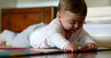 Sevimli bebek yerde uzanmış oyun halısına dokunarak dünyayı keşfediyor.