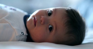 Sevimli bebek yatakta uzanmış, kamera portresine bakıyor.