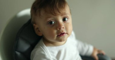 Kameraya gülümseyen sevimli bir bebek. Sandalyeye oturan erkek bebeğin portresi.