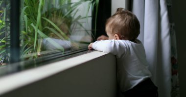 Sevimli bebek ayakta durmayı öğreniyor pencereye yaslanıyor dışarıya bakıyor ele uzanıyor