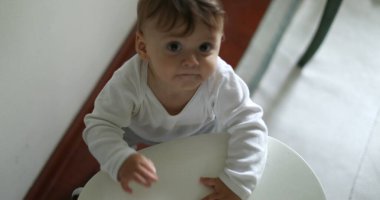 Kameraya bakan sevimli bir bebek. Bebek bebek sandalyeyi tutuyor.