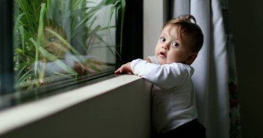 Evinin penceresinden sarkan sevimli bir erkek bebek. Bebek gülümseyen portre