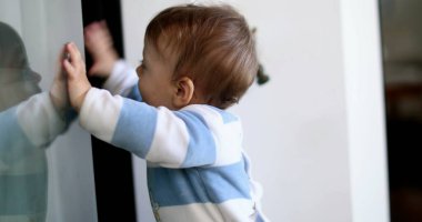 Küçük çocuk cam yansımasına yaslanıyor. Bebek pencerede duruyor.