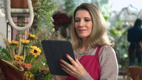 オンライン注文をチェック赤いエプロンを身に着けているデジタルタブレットを保持している花店の女性ビジネスオーナーの肖像 — ストック写真