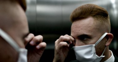 Cerrahi maske takan, yüzünü parmaklarıyla ovuşturan bir adam.