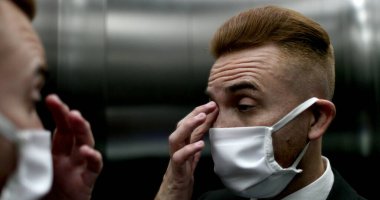 Cerrahi maske takan, yüzünü parmaklarıyla ovuşturan bir adam.