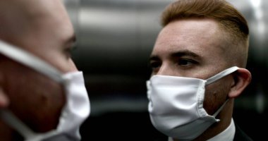 İşe giderken asansör aynasında yüz maskesi takan bir iş adamı.