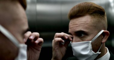 İş adamı maske takıyor asansör aynasında kendine bakıyor, koruyucu maskeyle dışarı çıkıyor.