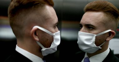 Asansörün içinde Covid-19 maskesi takan bir iş adamı aynaya bakan salgın maskesi takan biri.