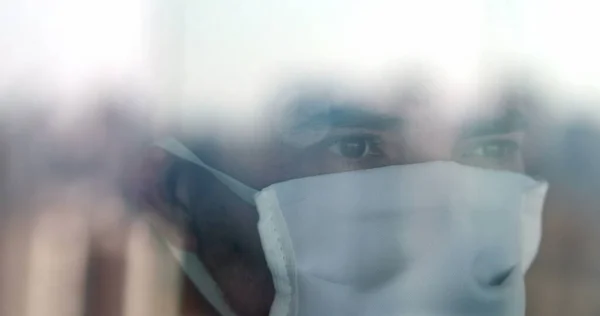 Person seen through glass window reflection with covid-19 surgical mask