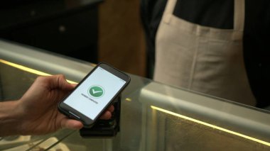 Müşteriler, iş yerindeki akıllı telefon cihazının NFC ödeme teknolojisiyle ödeme yapıyorlar.