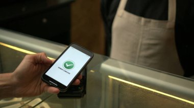 Müşteriler, iş yerindeki akıllı telefon cihazının NFC ödeme teknolojisiyle ödeme yapıyorlar.