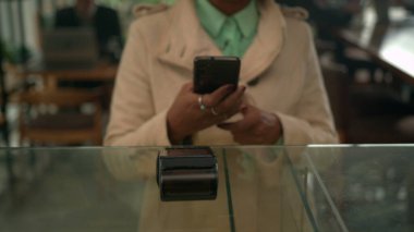 Tezgahta cep telefonuyla ödeme yapan siyah bir bayan müşteri var. Kahve dükkanında akıllı telefon cihazı ile NFC ödemesi