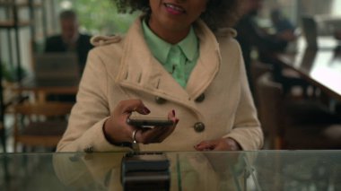 Tezgahta cep telefonuyla ödeme yapan siyah bir bayan müşteri var. Kahve dükkanında akıllı telefon cihazı ile NFC ödemesi