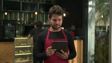 Genç işletme sahibi elinde tabletle kafede internetten siparişlere bakıyor.