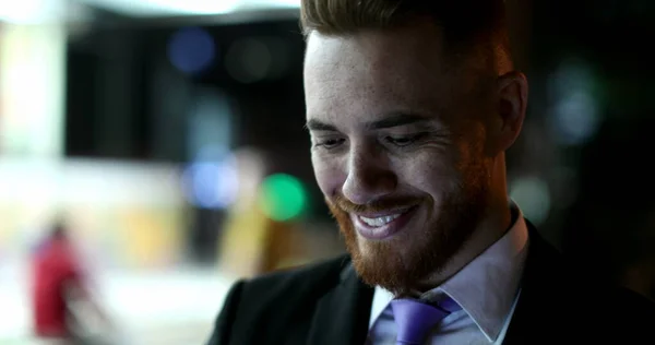 Business man face walking at night looking at smartphone smiling