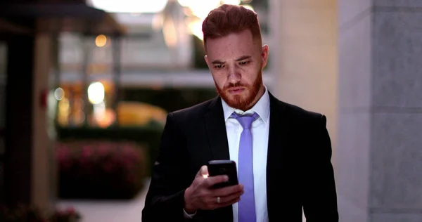 Business man checking cellphone at night walking in corporate center