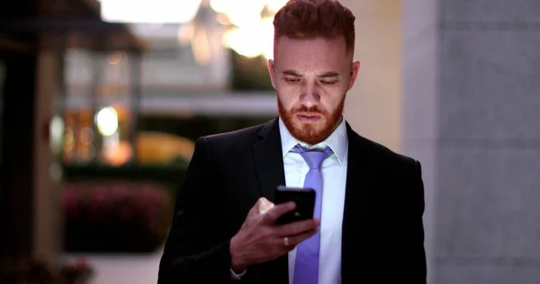 Business man checking cellphone at night walking in corporate center