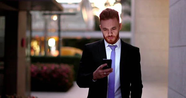 Business man checking cellphone at night walking in corporate center