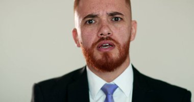 Kızgın adam tartışırken kameraya bakıyor. İş elbisesi giymiş üzgün biri kamerayla konuşuyor.