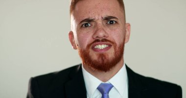 Kızgın adam tartışırken kameraya bakıyor. İş elbisesi giymiş üzgün biri kamerayla konuşuyor.