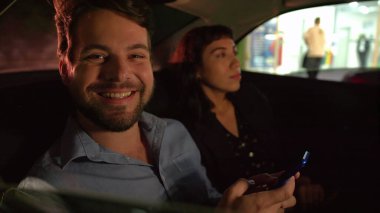 Gece işten sonra arabanın arka koltuğunda elinde akıllı telefon cihazıyla gülümseyen mutlu bir adam. Taksinin içinde iki kişi.