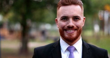 Dışarda duran bir iş adamı gülümsüyor. Kızıl saçlı yakışıklı yönetici.