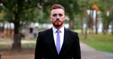 Dışarda duran bir iş adamı gülümsüyor. Kızıl saçlı yakışıklı yönetici.