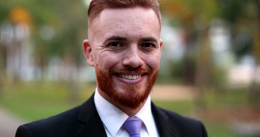 Dışarda duran bir iş adamı gülümsüyor. Kızıl saçlı yakışıklı yönetici.