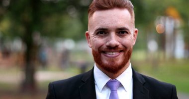 Dışarda duran bir iş adamı gülümsüyor. Kızıl saçlı yakışıklı yönetici.