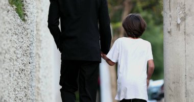 Baba, kaldırımda yürüyen çocukla el ele tutuşuyor.