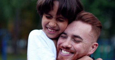 Baba ve oğul kucaklaşıyorlar. Birbirlerine sarılıyorlar. Beyaz baba ve melez çocuk.