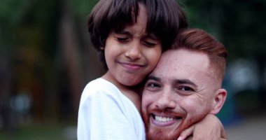 Baba ve oğul kucaklaşıyorlar. Birbirlerine sarılıyorlar. Beyaz baba ve melez çocuk.