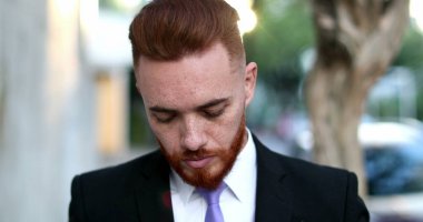 Yakışıklı yönetici kameraya gülümsüyor, İrlandalı kızıl saçlı erkek dışarıda bekliyor.