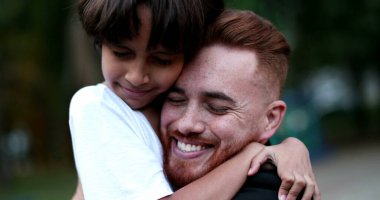 Ebeveyn ve çocuk kucaklaşır ve kucaklaşır. Baba ve genç çocuk farklı etnik çeşitlilikte sevgi ve özen, otantik